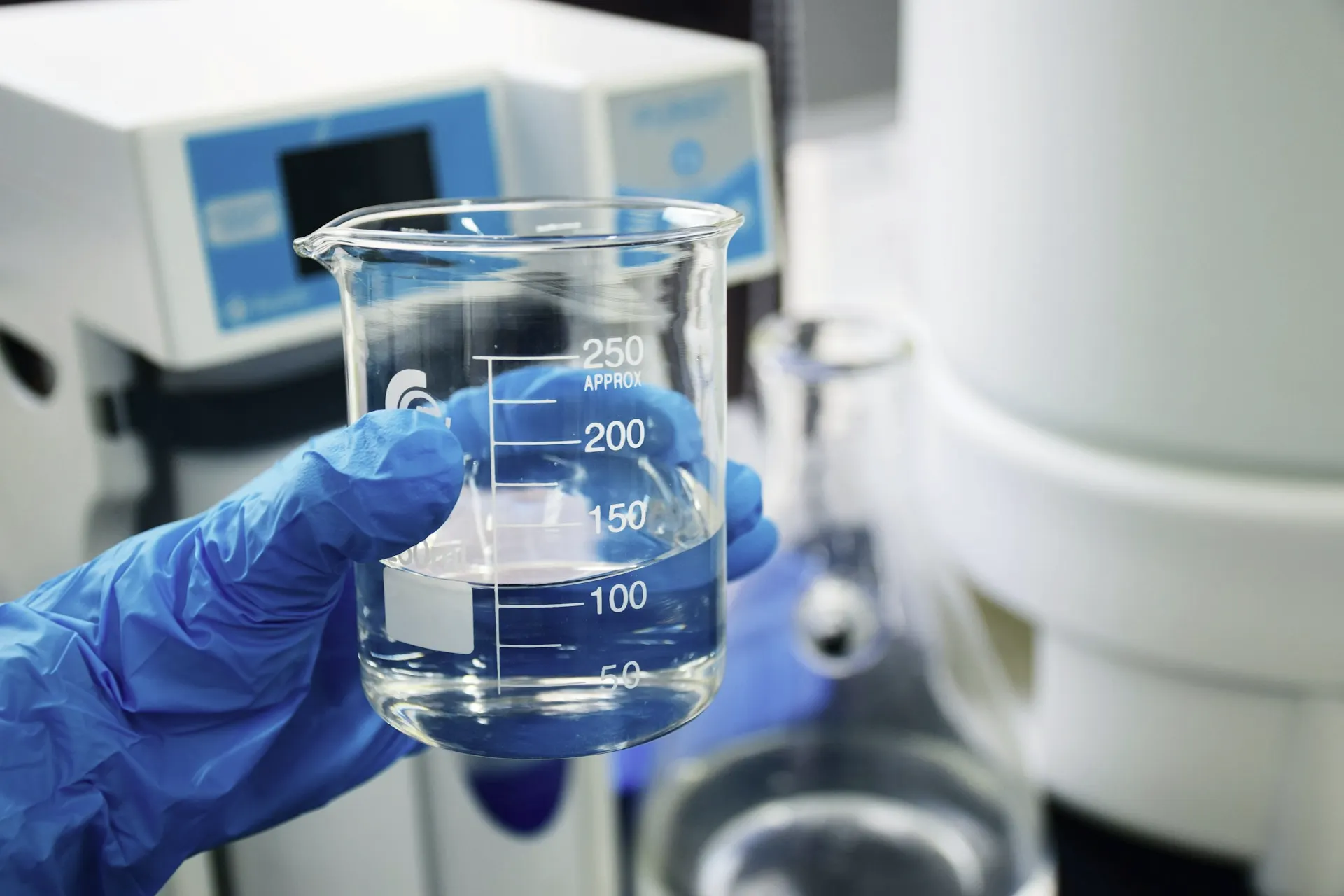 Industry context: Gloved hand holding a laboratory beaker of clear liquid.